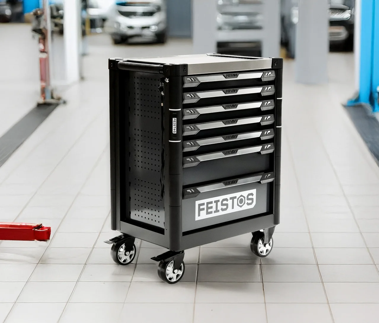 Schwarzer FEISTOS Werkstattwagen mit silberner Oberseite und mehreren Schubladen, steht auf Fliesenboden in einer Werkstatt.