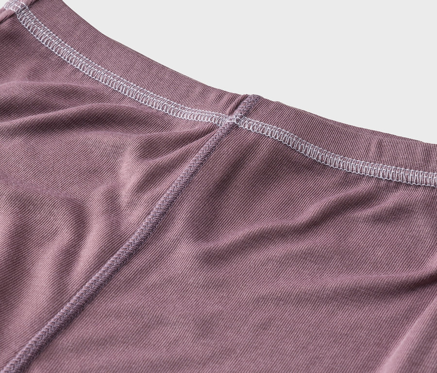 Nahaufnahme eines mattvioletten Rippstoffs mit weißen Nähten am oberen Rand und einer violetten Naht in der Mitte.