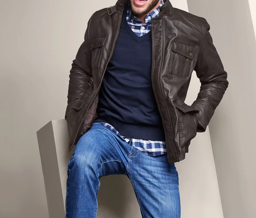 Ein lachender Mann sitzt auf einem weißen Sockel und trägt eine Lederjacke.