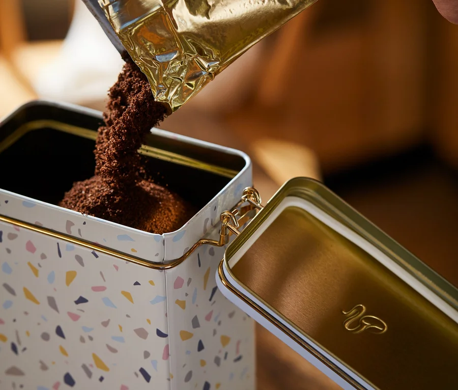 Kaffee wird in eine Kaffeedose mit Terrazzo-Muster geschüttet.