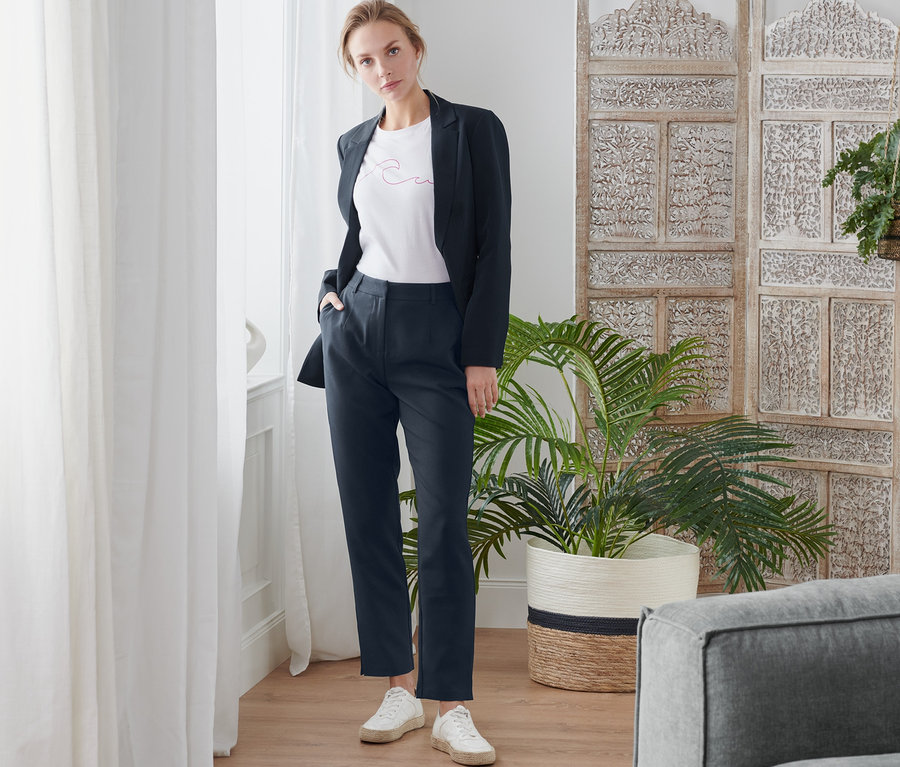 Frau posiert in dunklem Blazer und Webhose.