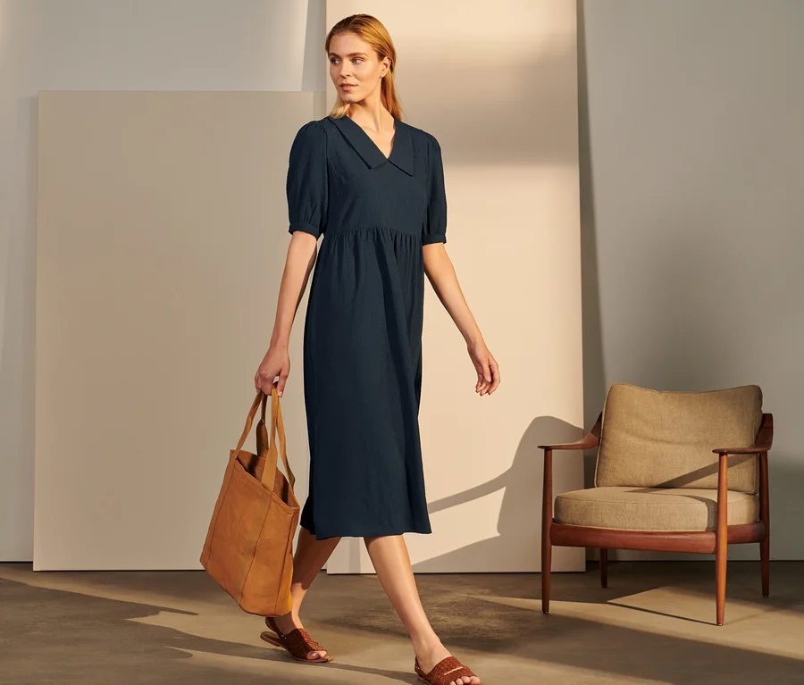 Frau geht und trägt eine braune Tasche, sie trägt ein gekrepptes Blusenkleid.