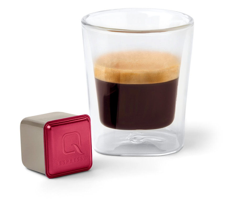 Auf einem weißen Hintergrund steht ein Glas Espresso neben einer Kapsel Qbo Espresso SIDAMA ROYAL.
