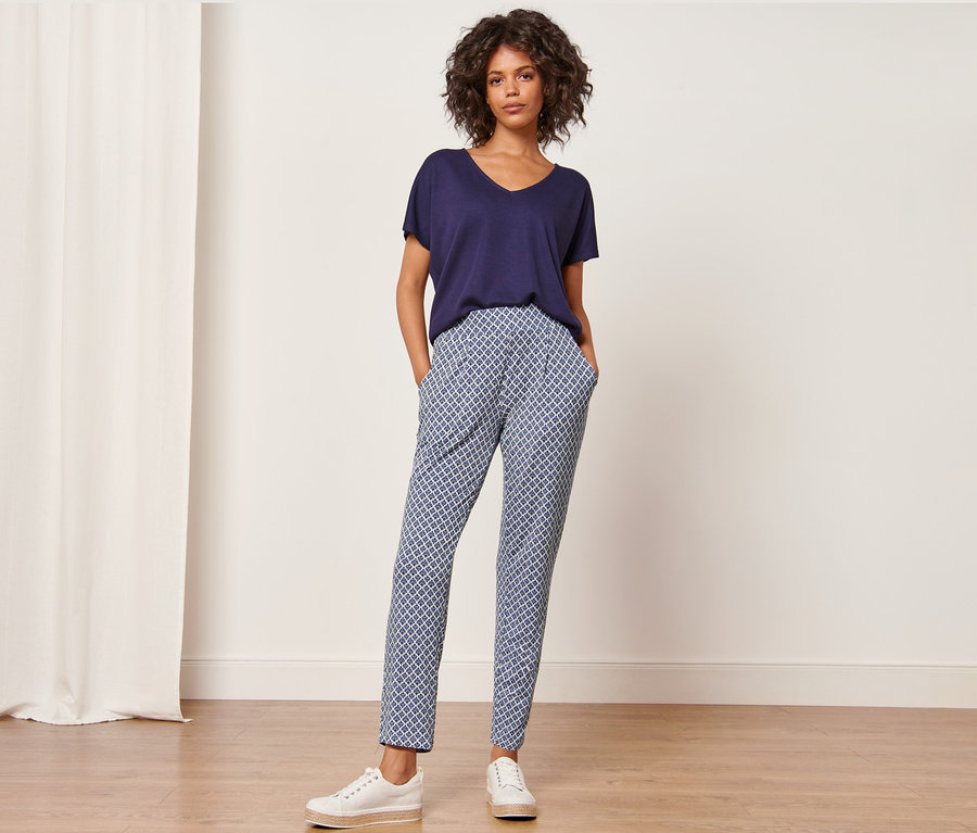 Frau steht mit Händen in den Taschen der bedruckten Jerseyhose.