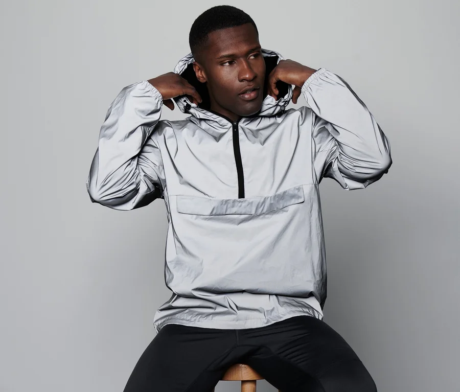 Mann sitzt auf einem Hocker und zieht einen reflektierenden Windbreaker an.