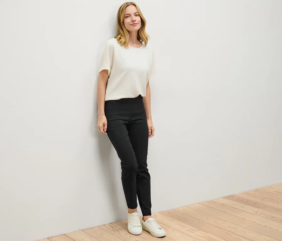 Eine Frau lehnt an einer Wand und trägt eine schwarze Stretchhose.