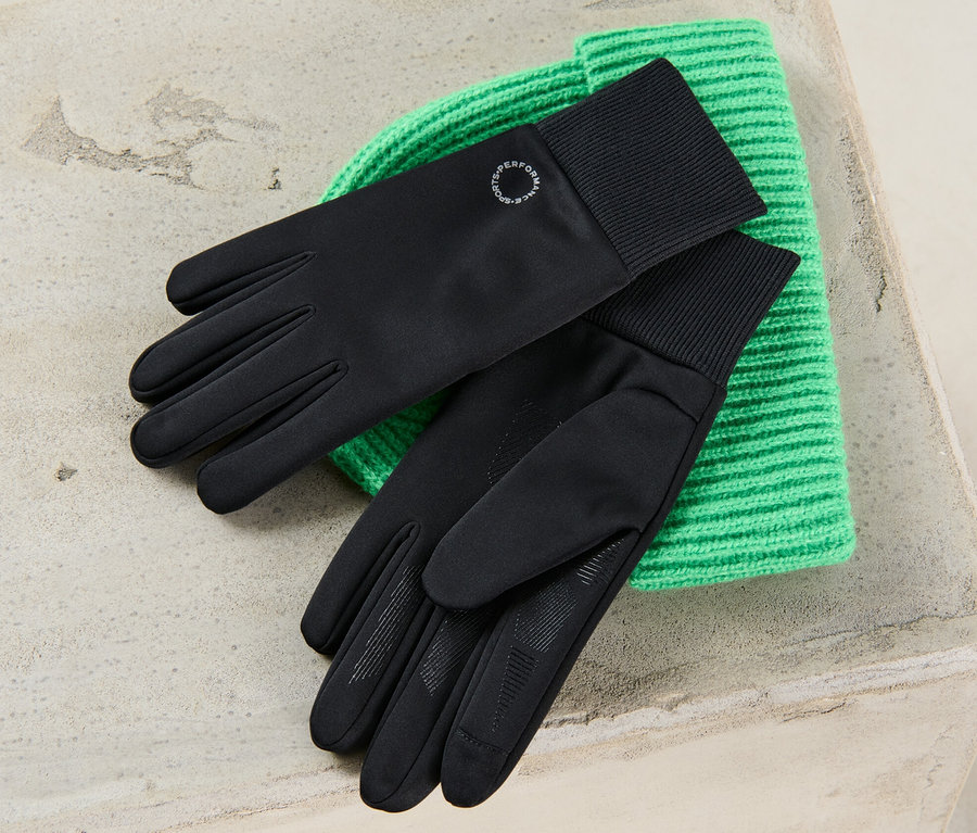 Schwarze Windprotection-Handschuhe liegen auf einer grünen Strickmütze.