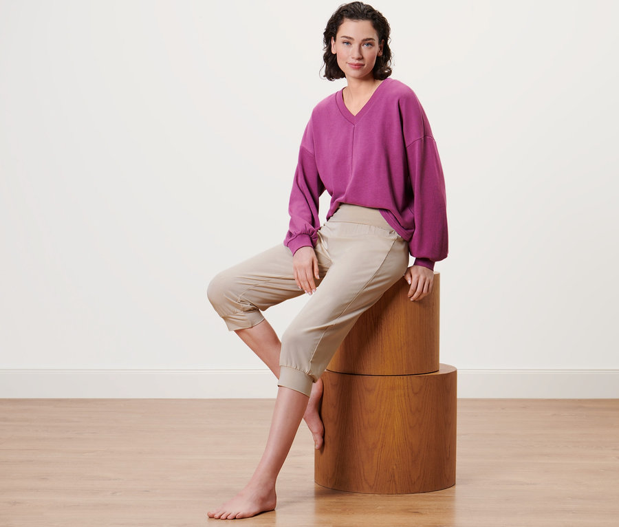 Frau sitzt auf einem Holzsockel und trägt eine beige 3/4-Yogahose.