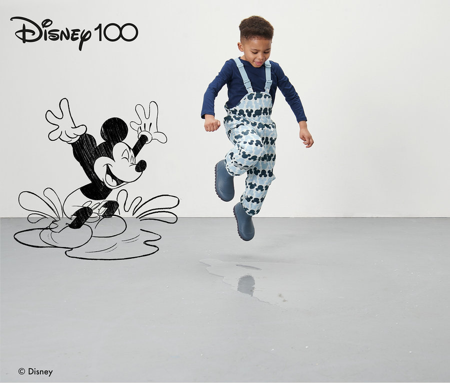 Junge springt auf grauem Boden in blauer Kleinkind-Thermo-Regenhose »Micky« mit Mickey Mouse-Muster.