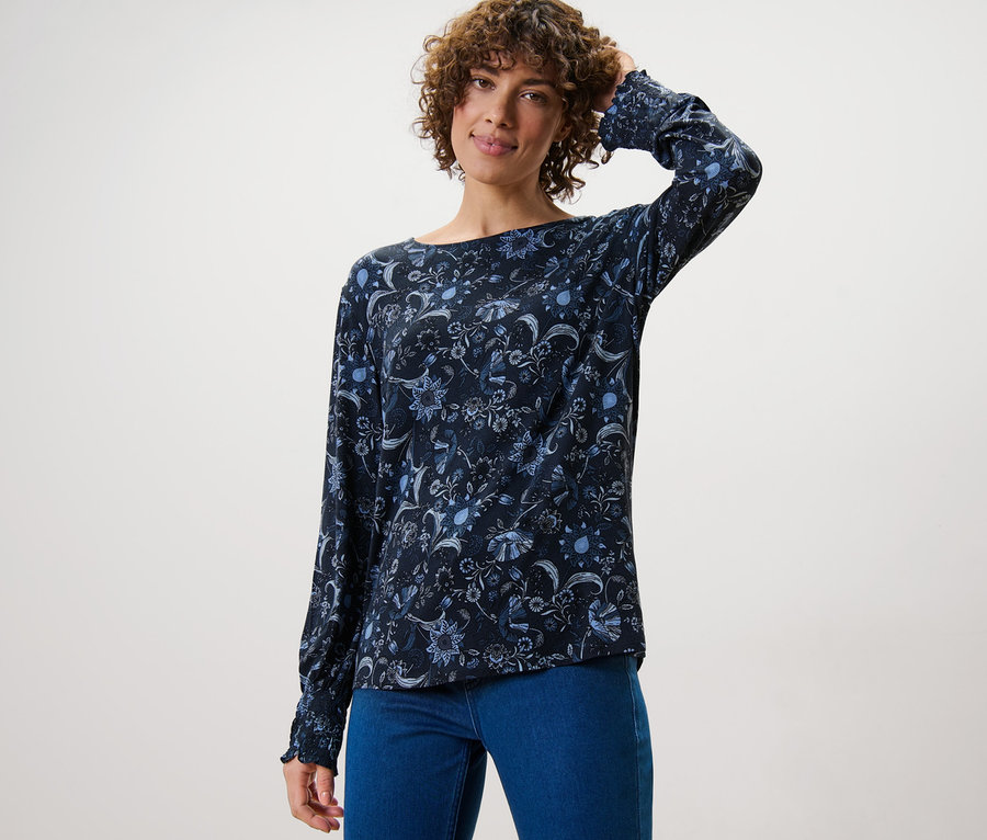Frau posiert in einem bedruckten Blusenshirt und Jeans.