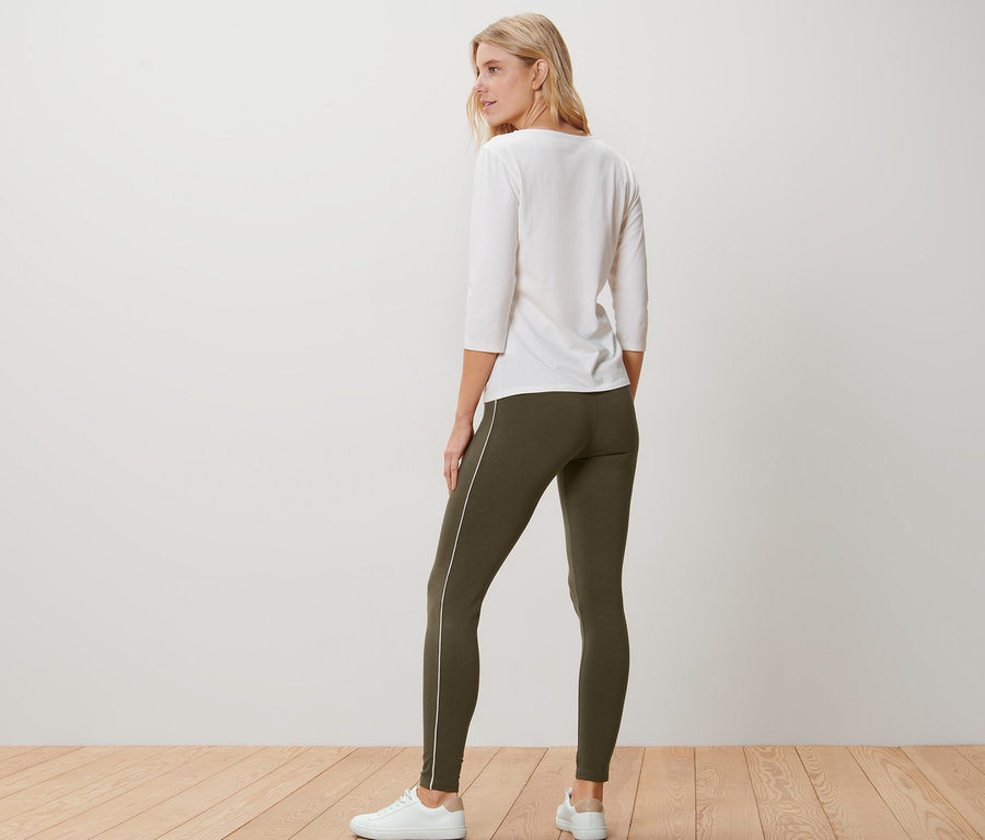 Frau von hinten trägt eine weiße Bluse und olivgrüne Leggings mit Paspelierung.
