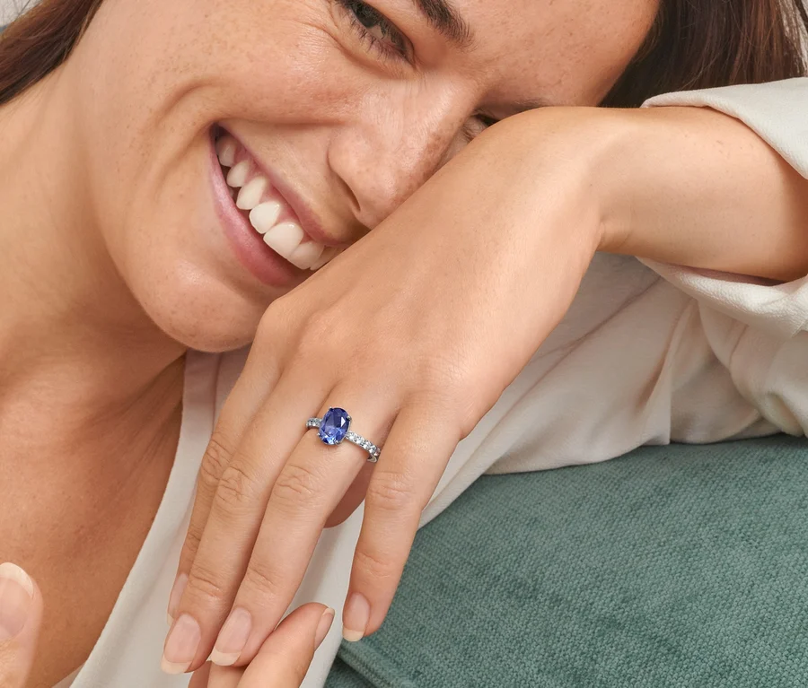 Lächelnde Frau mit Ring aus 925er Silber, rhodiniert, mit blauem Kristall und Zirkonia und Ohrsteckern aus 925er Silber, rhodiniert, mit blauem Kristall und Zirkonia.