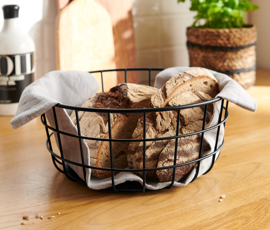 Brot in einer Drahtschale mit Stoffeinlage auf einer Holzplatte.