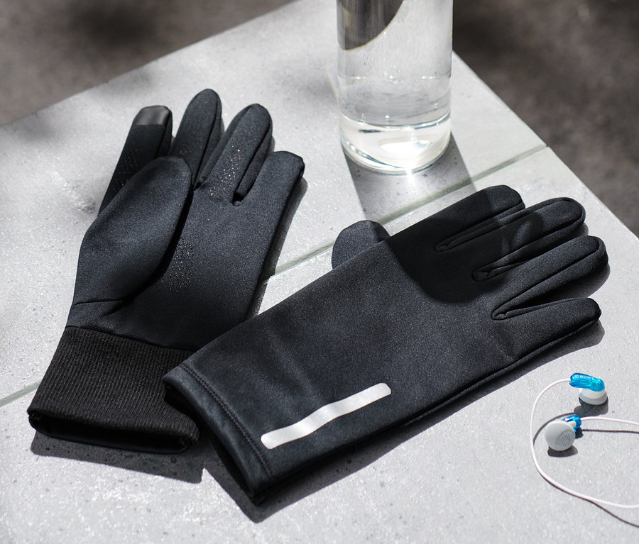 Zwei schwarze Windprotection-Thermohandschuhe, eine Wasserflasche und Kopfhörer liegen auf einer grauen Oberfläche.