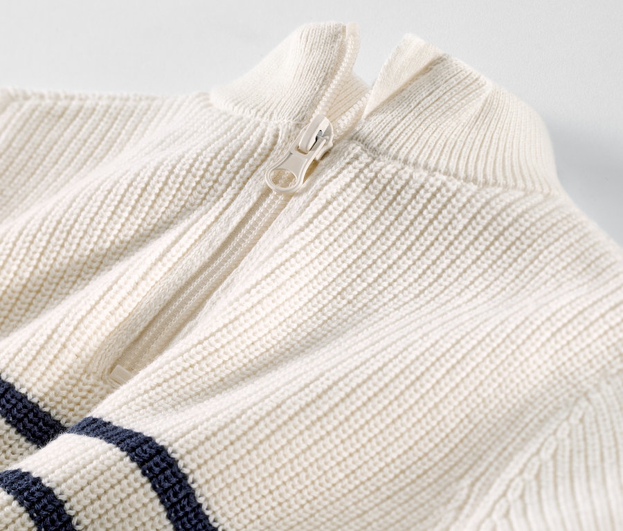 Detailaufnahme eines Kinder-Troyers mit weißem Reißverschluss und dunkelblauen Streifen.