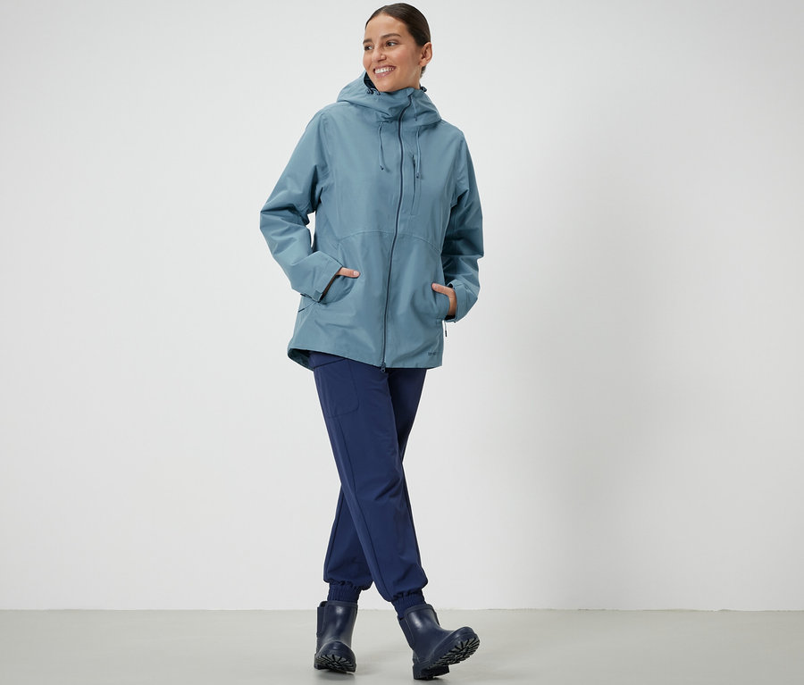 Frau steht und posiert in einer hellblauen Funktions-Outdoorjacke.