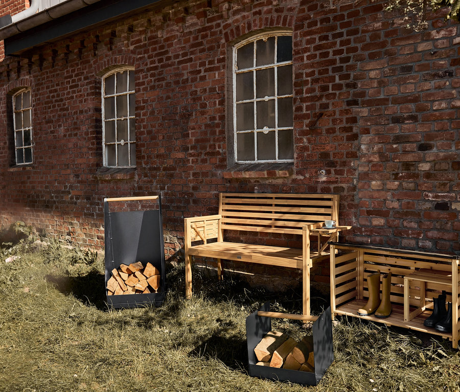 Ein Outdoor-Schuhregal, eine Holzbank und zwei Holzscheitkörbe stehen auf einem Rasen vor einem Backsteingebäude.
