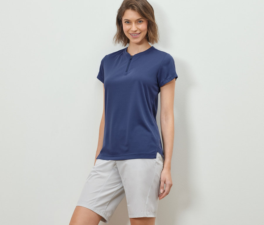 Frau posiert in einem Half-Zip-Sportshirt und Shorts.