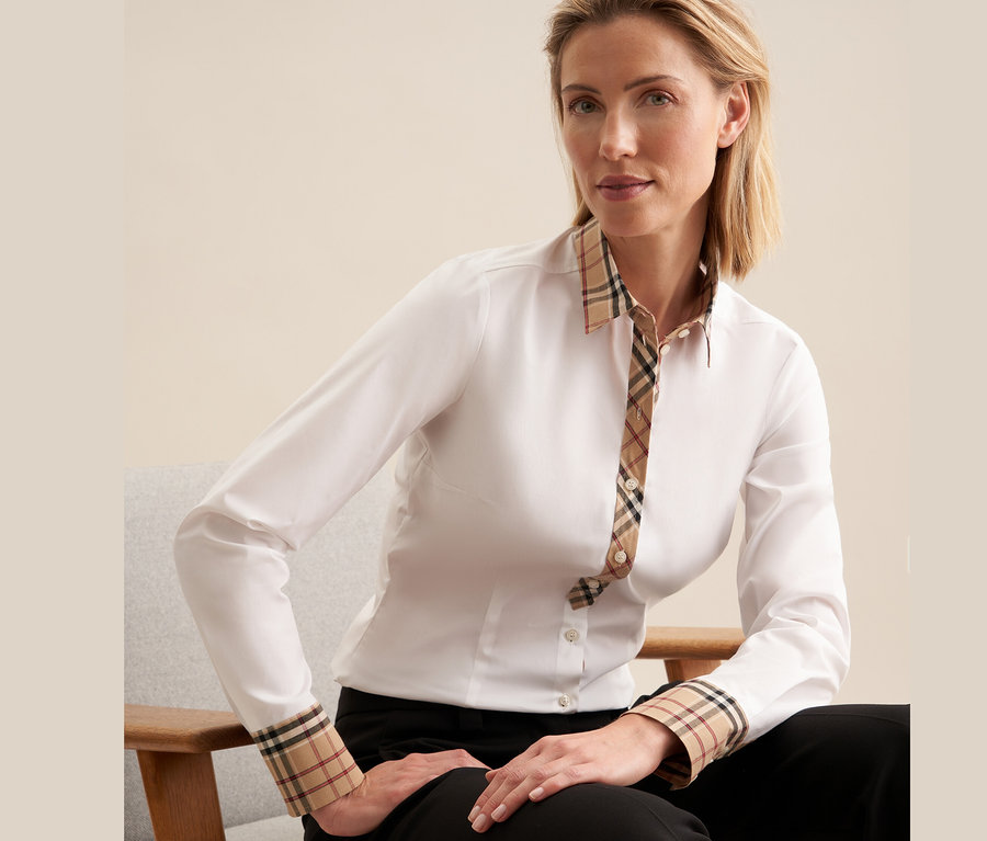 Frau sitzt auf einem Stuhl und trägt eine weiße Seidensticker Popeline-Bluse mit Karodetail.