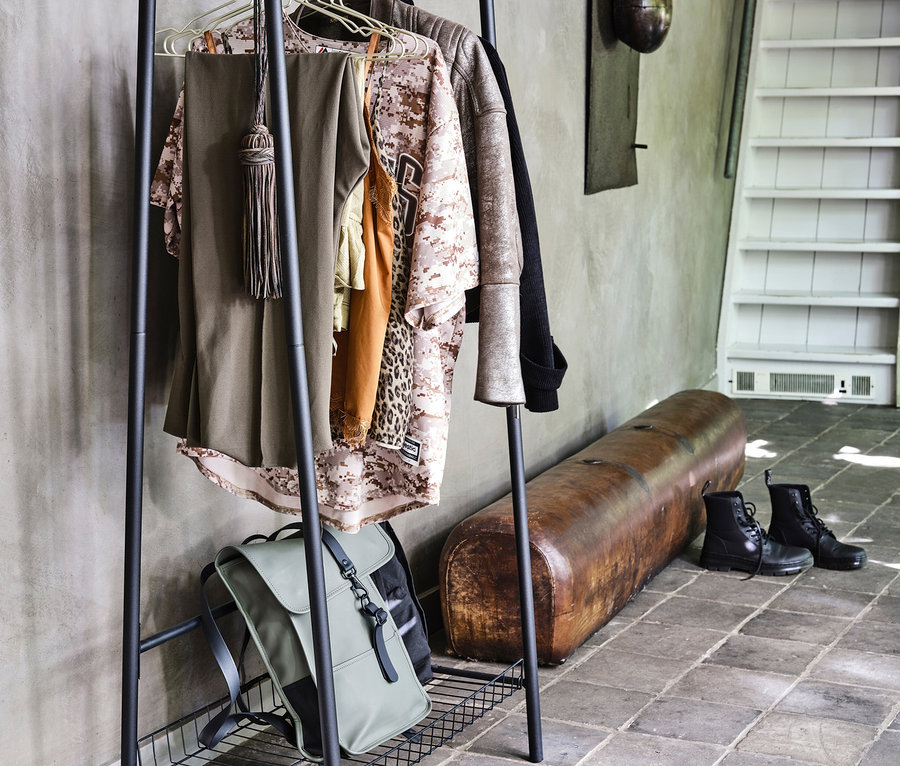 Schwarze Kleidung hängt auf einem schwarzen Woood Metall-Kleiderständer »Jovi«, darunter ein Rucksack.
