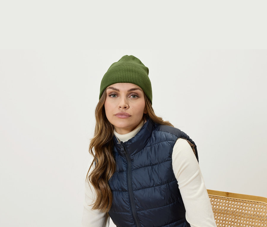 Porträt einer Frau mit braunen Haaren, olivgrüner Mütze und dunkelblauer Steppweste.