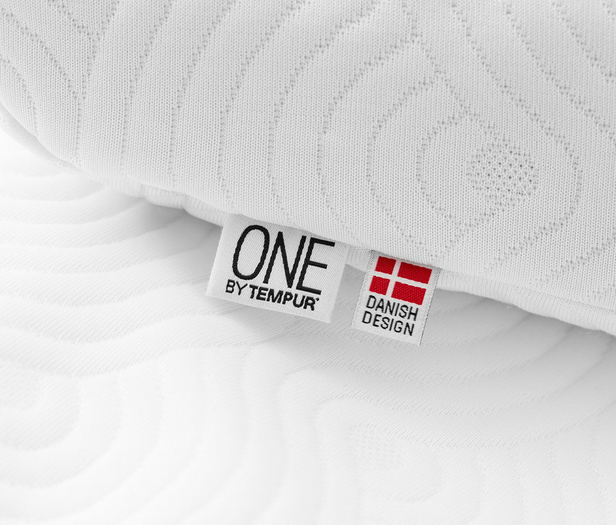 Detailansicht eines weißen TEMPUR ONE® Support Kissens mit einem Etikett, das 'ONE by TEMPUR' und 'Dänisches Design' zeigt.