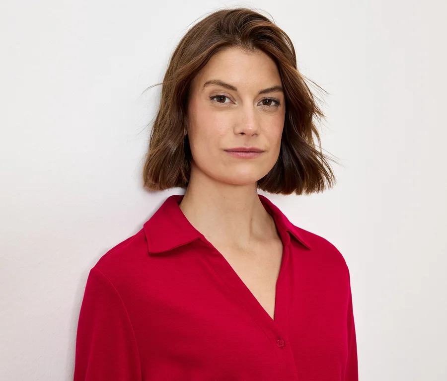 Porträt einer Frau mit braunen Haaren in einer roten Bluse mit Kragen.