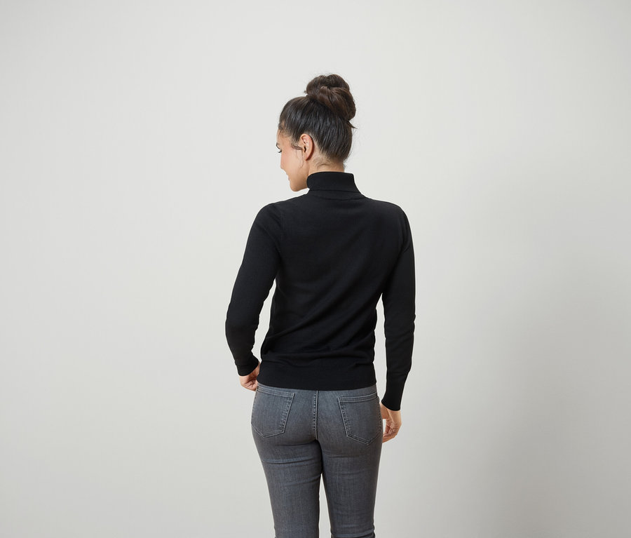 Rückansicht einer Frau mit Duttfrisur, die einen schwarzen Rollkragenpullover und graue Jeans trägt.