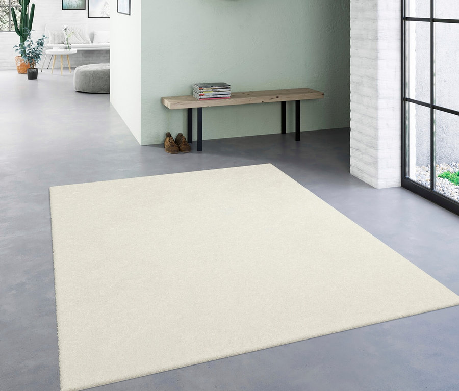 Ein wollweißer Teppich »Mellow« liegt in einem Flur. Im Hintergrund eine Bank mit Schuhen und Spiegel.