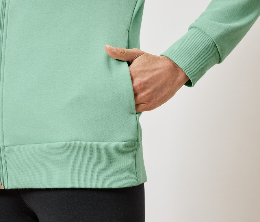 Detail einer hellgrünen Damen-Reißverschlussjacke mit Hand in der Tasche.