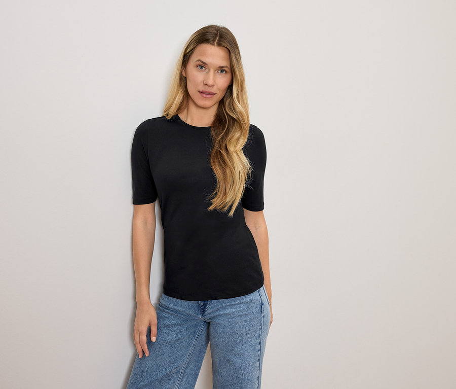 Frau mit blonden Haaren posiert in einem schwarzen T-Shirt und blauen Jeans.