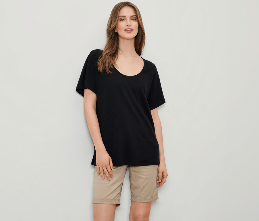 Eine Frau trägt ein schwarzes Shirt aus Leinenmix und eine beige Shorts.
