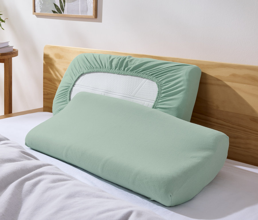 Zwei grüne Jersey-Nackenkissenbezüge liegen auf einem Bett.