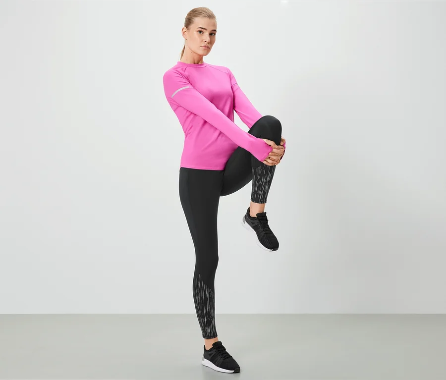 Frau dehnt Bein in schwarzen Leggings und rosafarbenem Oberteil.