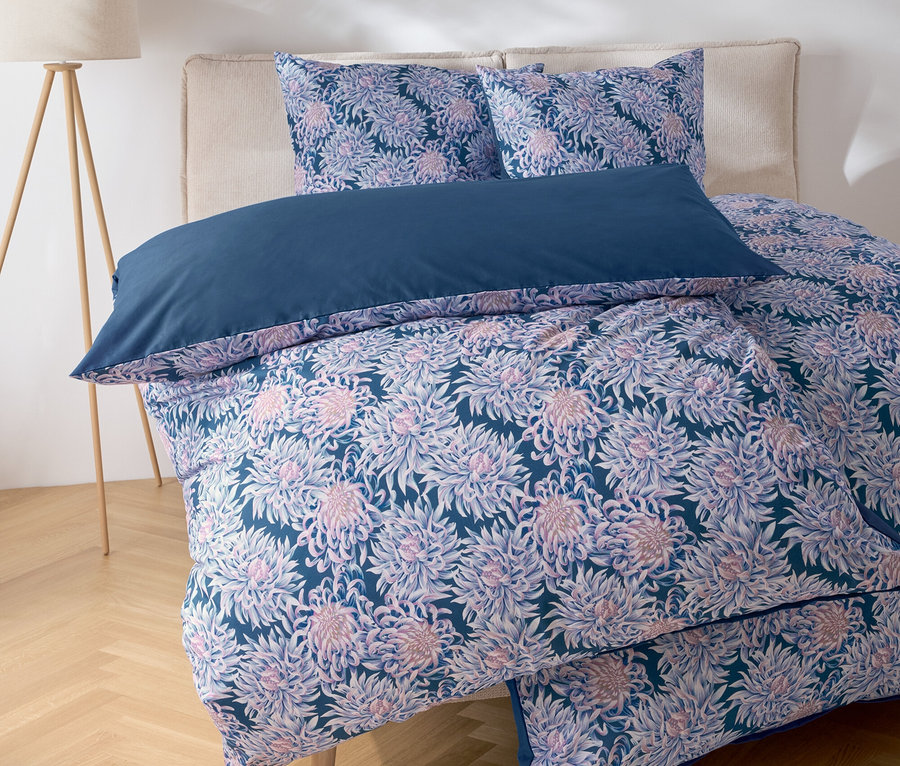 Detailansicht eines Bettes mit floraler Bettwäsche und blauem Kissen.