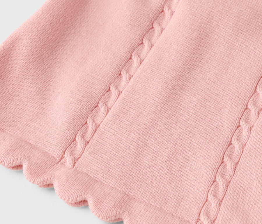 Nahaufnahme eines rosa Strickstoffes mit Zopfmusterdetails und gewelltem Saum.