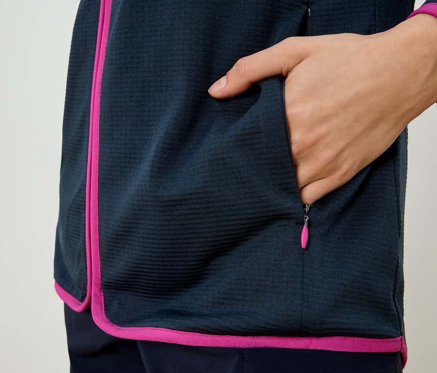 Person steckt Hand in die Reißverschlusstasche einer marineblauen Jacke mit pinkfarbenen Akzenten.