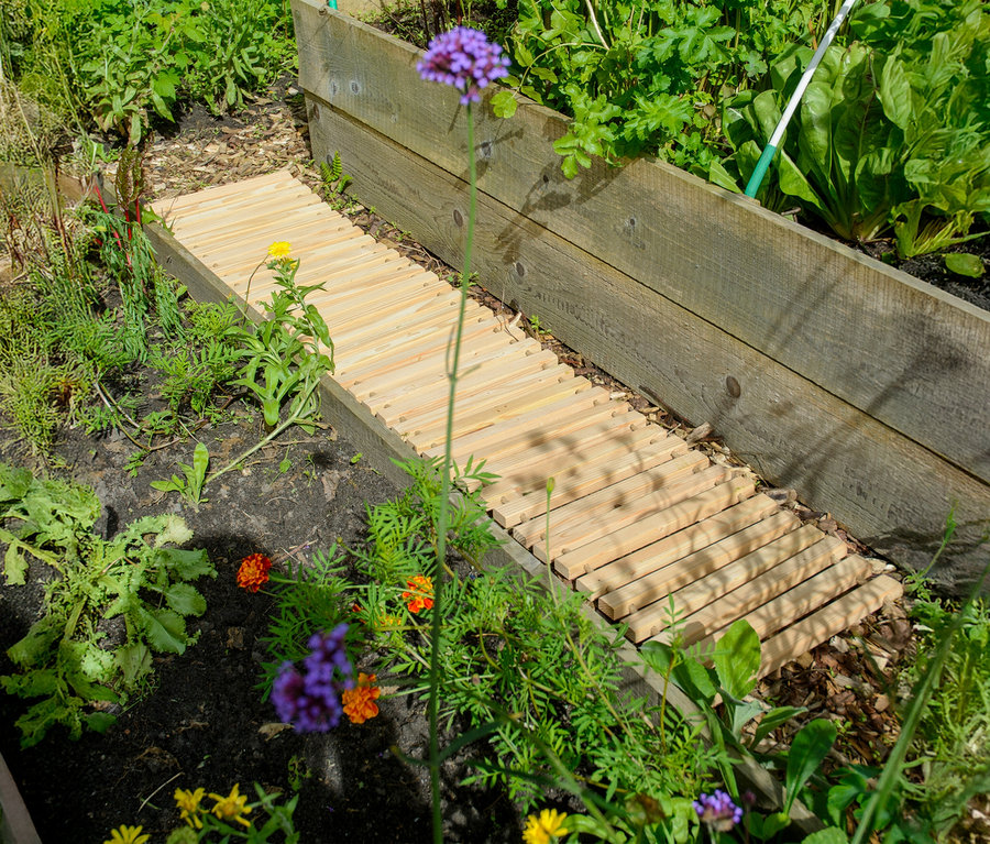 Holzsteg führt durch einen Garten mit Blumen und Gemüse.