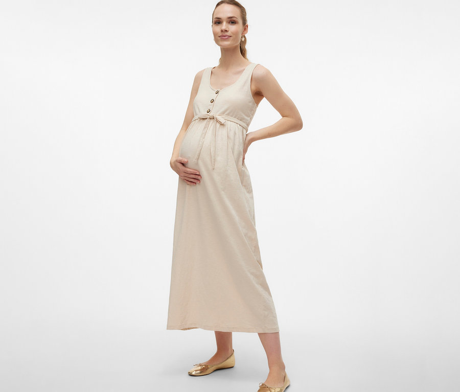 Schwangere Frau im MAMALICIOUS Schwangerschaftskleid »MLEVI LIA«, mit Gürtel und Knöpfen, posiert mit Händen an Bauch und Hüfte.