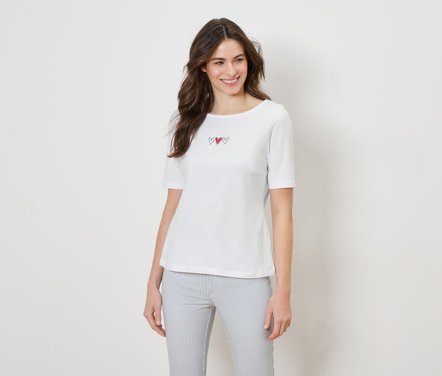 Frau trägt ein weißes T-Shirt mit drei Herzen und eine gestreifte Hose.
