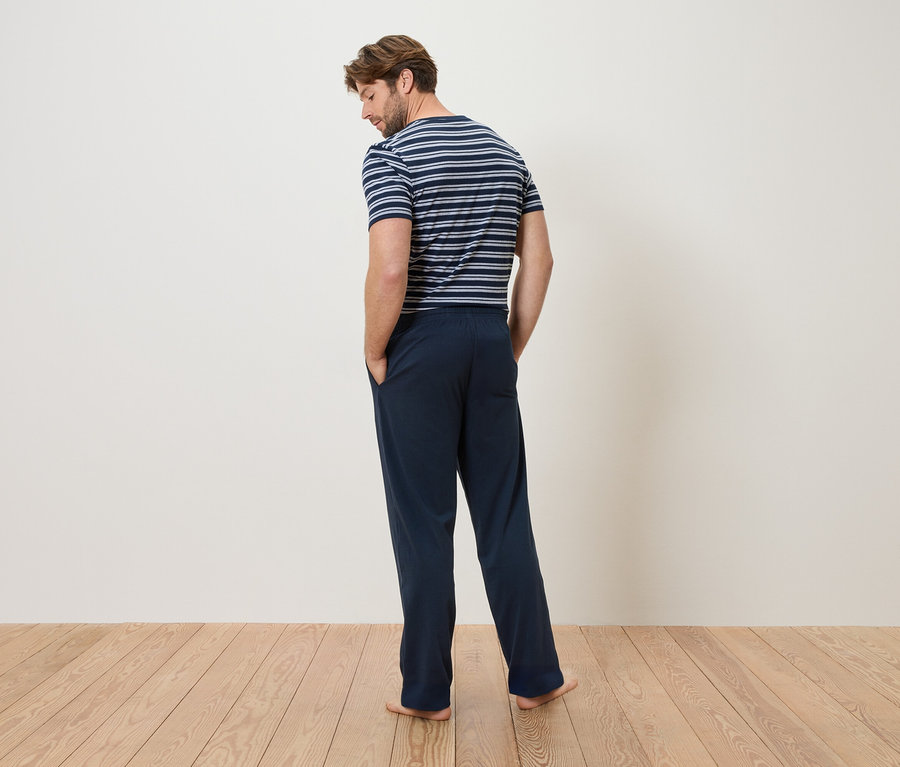 Mann von hinten in blau-weiß gestreiftem T-Shirt und blauer Hose, Hände in den Hosentaschen.