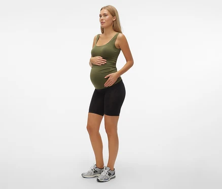 Schwangere Frau im olivgrünen Tanktop und schwarzen MAMALICIOUS Skinny Shorts »MLTIA JEANNE«, mellow buff, steht seitlich.