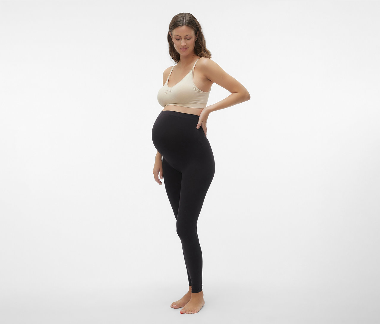 Schwangere mit schwarzer Leggings posiert mit einem MAMALICIOUS MLILJA FEED ME BRA 2-P NOOS in Beige.