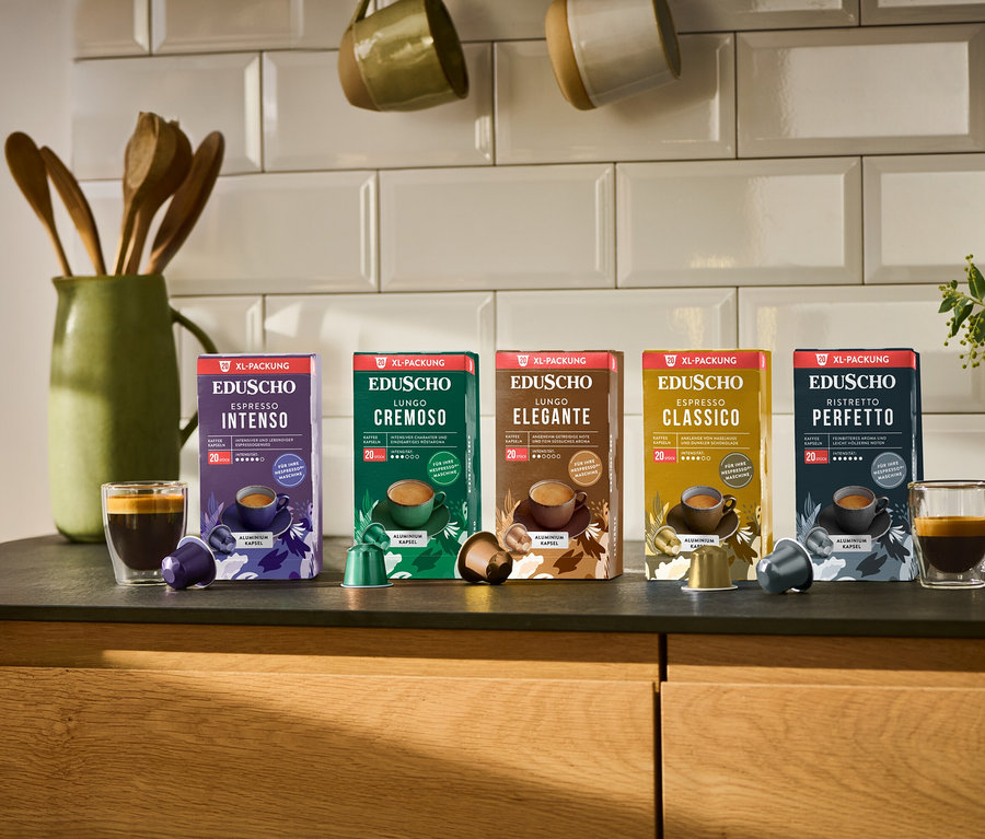 Fünf Packungen Eduscho Kaffeekapseln stehen auf einer Küchentheke, darunter Espresso Classico, Lungo Elegante, Lungo Cremoso, Ristretto Perfetto und Espresso Intenso.