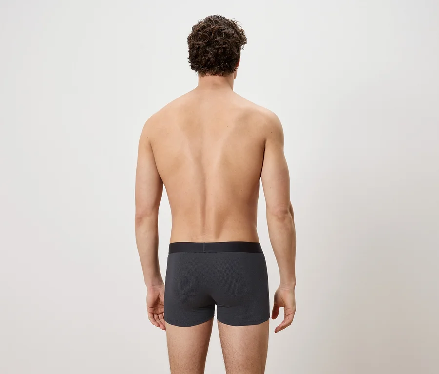 Mann mit lockigem Haar von hinten, der graue Boxershorts mit schwarzem Bund trägt.