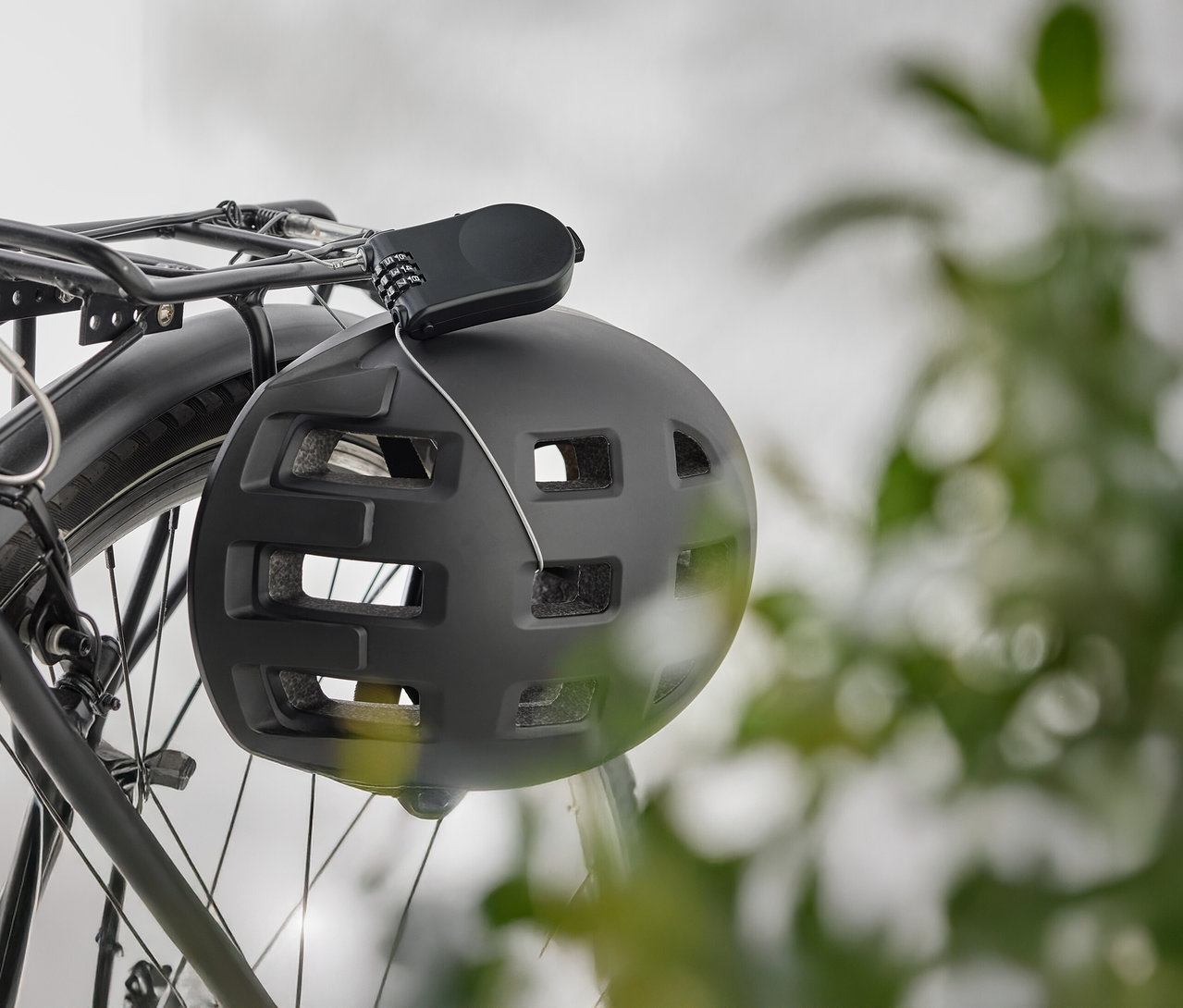 Ein schwarzer Fahrradhelm hängt mit einem Zahlenschloss an einem Fahrradgepäckträger.