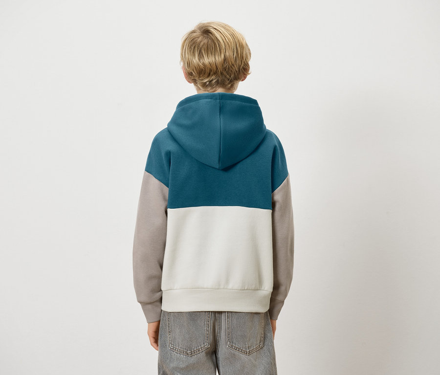 Rückansicht eines Kindes mit blonden Haaren, das einen Colour-Block-Hoodie in Blau, Grau und Weiß und graue Jeans trägt.
