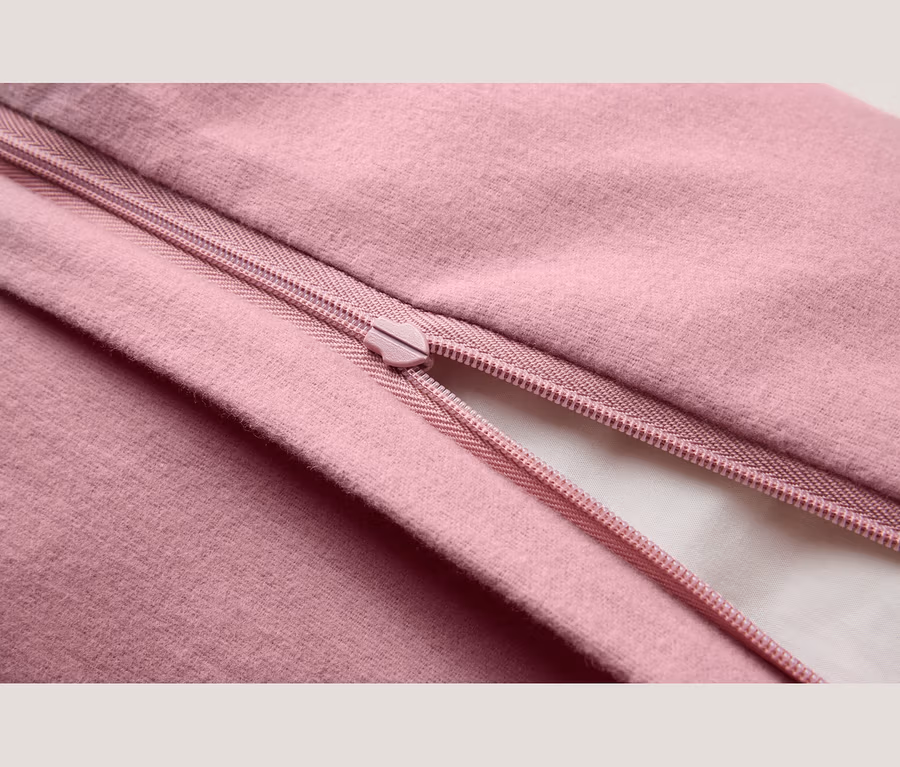 Nahaufnahme eines rosa Stoffes mit einem teilweise geöffneten rosa Reißverschluss, der ein weißes Futter darunter zeigt.