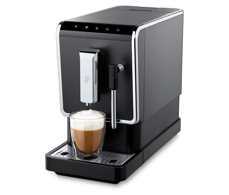 Ein anthrazitfarbener »Esperto Latte« Tchibo Kaffeevollautomat bereitet ein Getränk in einem Glas zu.