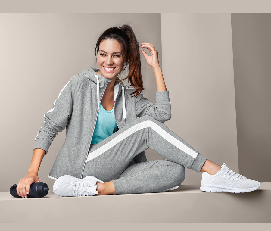 Frau sitzt und trägt eine graue Sweathose und weiße Turnschuhe.